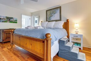 Een netjes opgemaakt bed met een houten hoofdbord, een nachtkastje met een lamp, en een schilderij aan de muur.