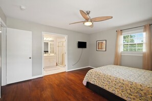 Un dormitorio con cama, ventilador de techo, televisor y ventana con cortinas.