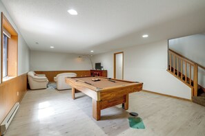 Ein Billardtisch in einem Raum mit Holzboden, einer Couch und einer Treppe.