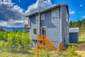 A two-story house with a wooden staircase, a fenced yard, and a mountain backdrop. - Blue Sky Retreat w/ 3rd-Floor Mtn Views, Starlink (Bailey)