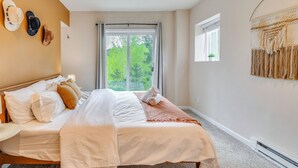 Ein Schlafzimmer mit einem großen Bett, einem Fenster mit Blick auf Bäume und einem an der Wand hängenden Kunstwerk.