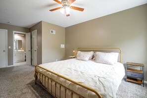 Una camera da letto con un letto, un comodino, una lampada da comodino, una ventola a soffitto e una porta che dà su un bagno.