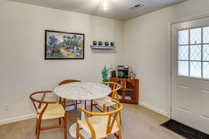 A dining area with a round table and four chairs, a coffee station with a coffee maker and cups, a shelf with decorative items, and a door with a window. - Remote Work Ready! Walkable Fayetteville Home (Fayetteville)