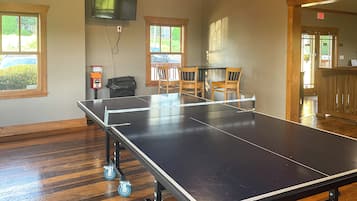 Une table de ping-pong sur roulettes, un téléviseur fixé au mur et une fenêtre donnant sur une voiture et de la verdure.