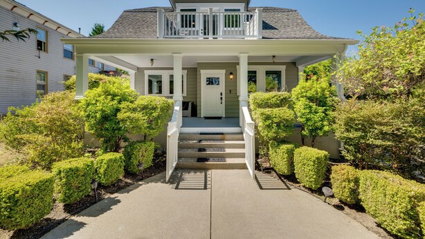 Ein zweistöckiges Haus mit Veranda, einer Treppe zum Eingang und einem gepflegten Garten.