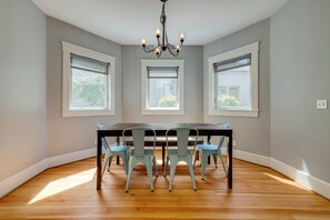 Une salle à manger avec une table en bois et quatre chaises, trois fenêtres et un lustre.