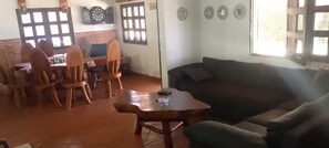 A living room with a dark-colored sofa, a wooden coffee table, and a dining area with wooden chairs and a brick wall. - Welcoming 3-bedroom house in Guatape perfect for your getaway (Guatape)