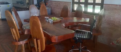 A dining area with a wooden table and chairs, a fruit bowl, and a window with a view.