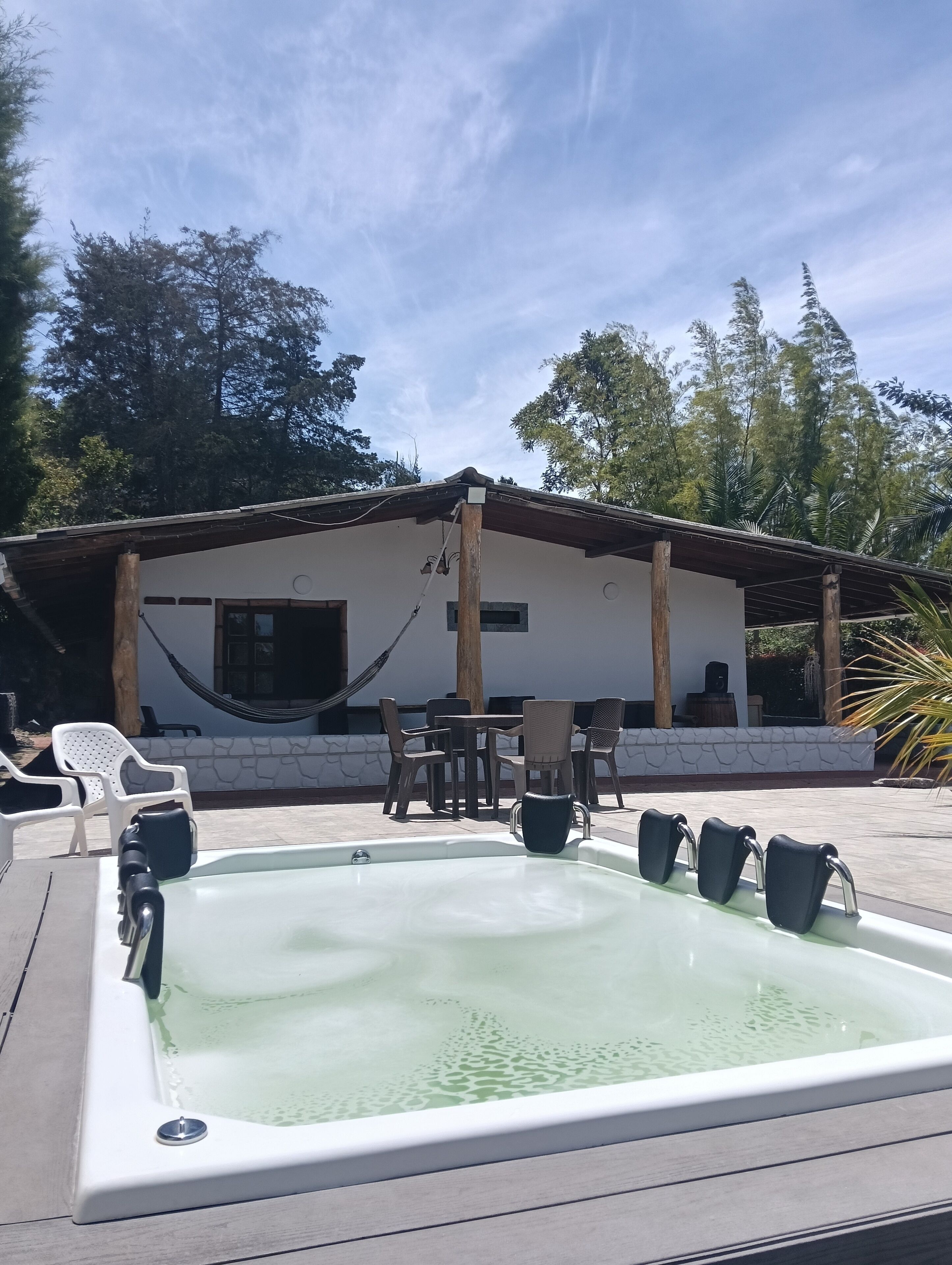 Ein Whirlpool mit Holzterrasse, ein weißes Gebäude mit einem Ziegeldach und Gartenmöbel.