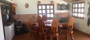 A dining area with wooden chairs and a table, a brick wall, and windows with blinds. - Welcoming 3-bedroom house in Guatape perfect for your getaway (Guatape)