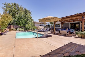 Ein Garten mit Swimmingpool, Liegestühlen, einer Pergola und einer überdachten Terrassenfläche.