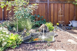 Ein Garten mit Teich, Pflanzen und einem Holzzaun.