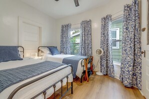 A bedroom with two beds, a bedside table, a fan, and patterned curtains.