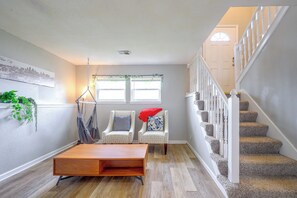A hallway with a wooden coffee table, two patterned armchairs, a hanging chair, and a staircase with a white railing. - 11 Mi to Overland Park: Olathe Mid-Term Stay (Olathe)