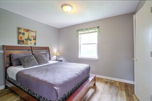 Un dormitorio con cama, mesita de noche, lámpara, ventana con persianas y decoración en la pared.