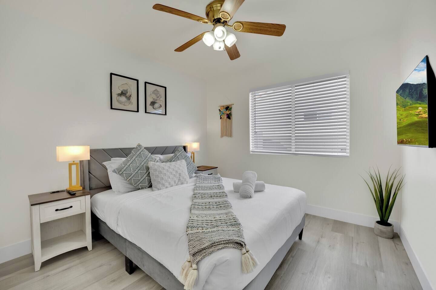 A bedroom with a bed, nightstands, a ceiling fan, a window with blinds, and a wall-mounted picture.