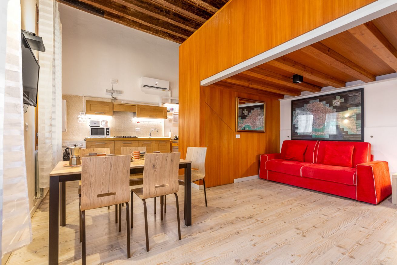 A modern interior with a dining area, kitchen, and a red sofa.