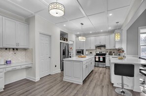 Une cuisine moderne avec des meubles blancs, un îlot central, des appareils en acier inoxydable et des luminaires suspendus.