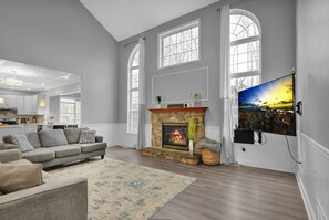 A spacious living room with a fireplace, a large window, and a television mounted on the wall. - 6 Beds 5,000 SqFt Country Retreat: Sleeps the Whole Family w/ Resort Pool & Spa (Mohnton)