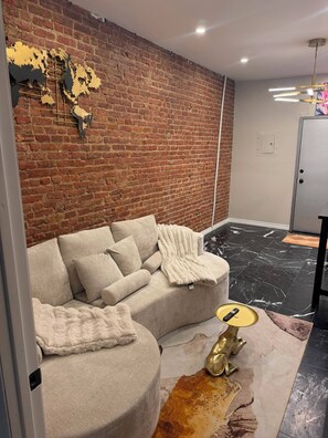 A modern living room with a brick wall, a sectional sofa, a gold statue, and a marble floor. - Cozy 1-bedroom apartment in lovely Brooklyn with AC (brooklyn)