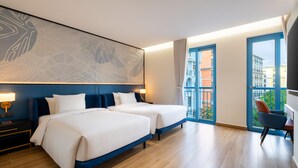 A hotel room with two beds, a large abstract wall art, a balcony with city views, and a desk with a chair. - AMÉRYS Hotel Phu Quoc (Phu Quoc)