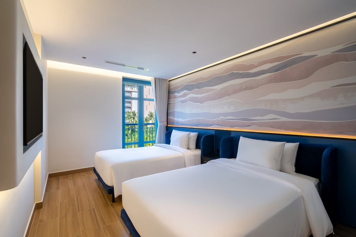 Ein Hotelzimmer mit zwei Betten, einem großen Fenster und einem Wandbild.