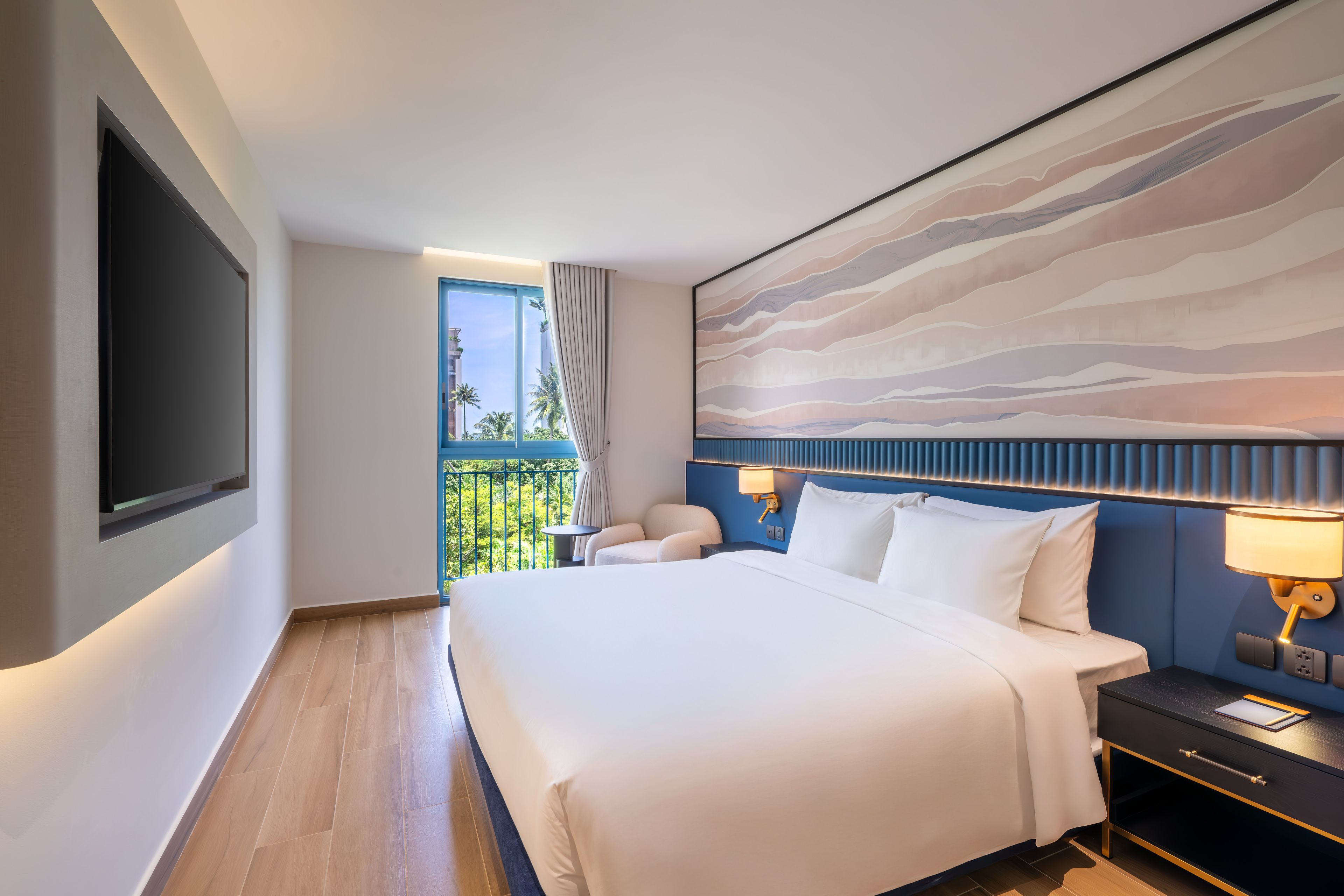 Habitació d'hotel amb un llit gran, televisió de pantalla plana, un balcó amb vistes a palmeres i un quadre abstracte modern a la paret.