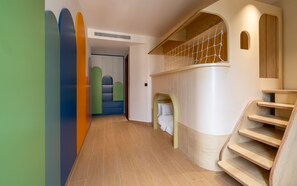 Ein modernes Interieur mit einer Holztreppe, einer gewölbten Wand mit Netzstruktur und einem Flur mit farbenfrohen geometrischen Wandverkleidungen.