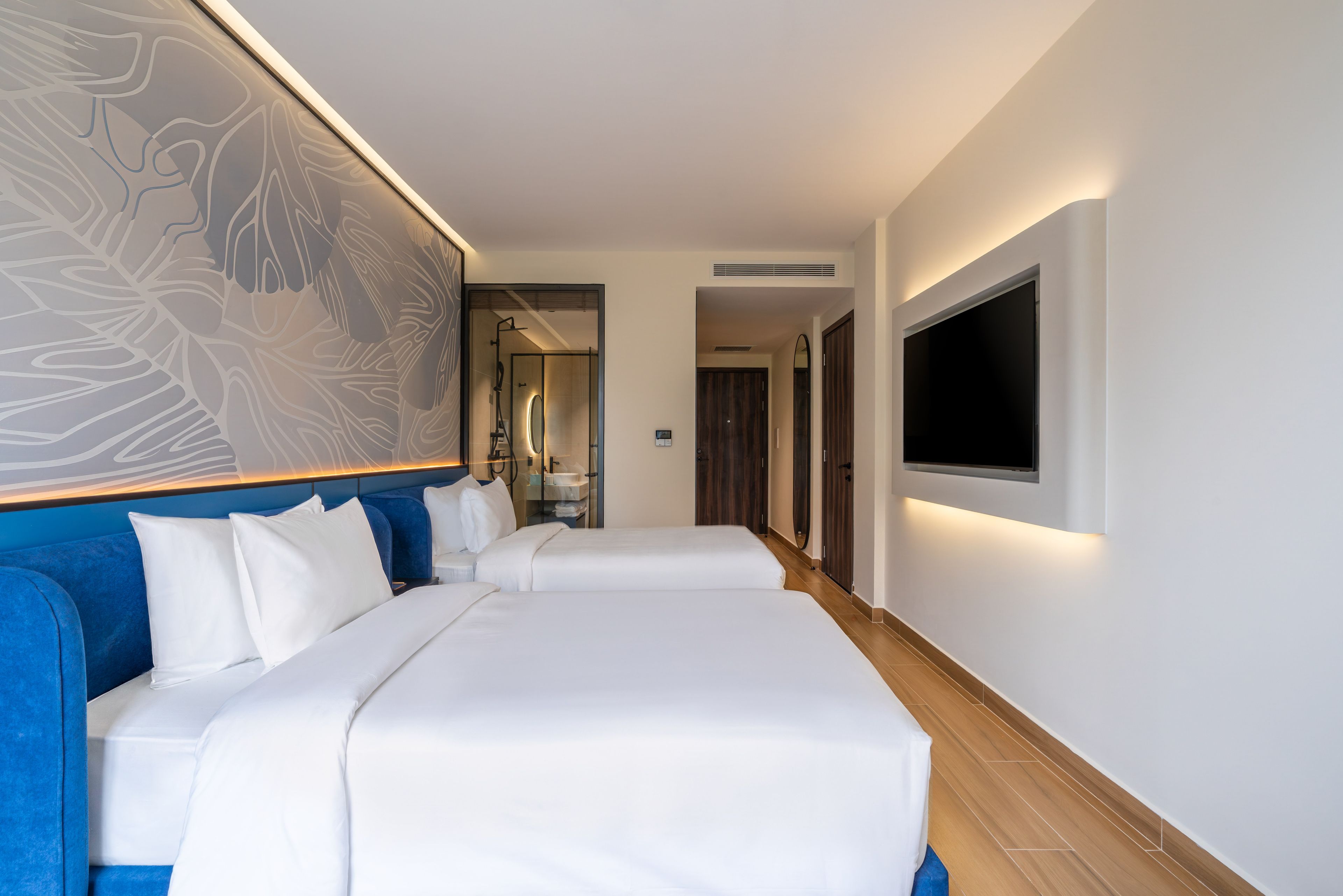 A hotel room with two beds, a large wall art piece, a flat-screen TV, and a bathroom visible through an open door.