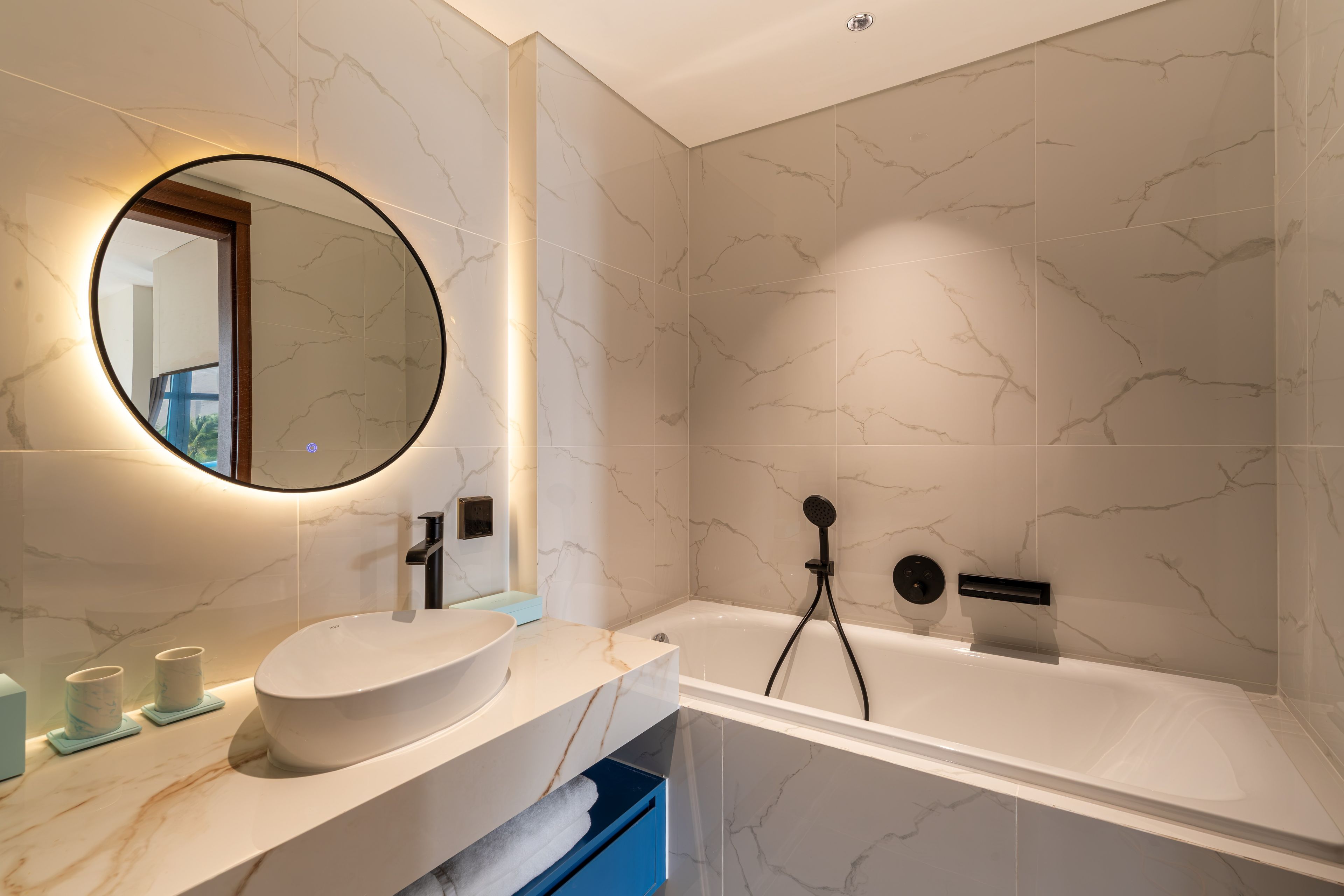 Un baño moderno con tocador de mármol, un espejo redondo, una bañera y un cabezal de ducha manual.