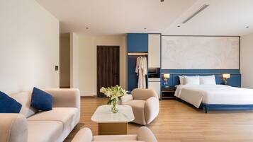 Quarto de hotel com sofá, poltrona, mesa pequena com flores, cama, mesa de cabeceira e mapa fixado na parede.