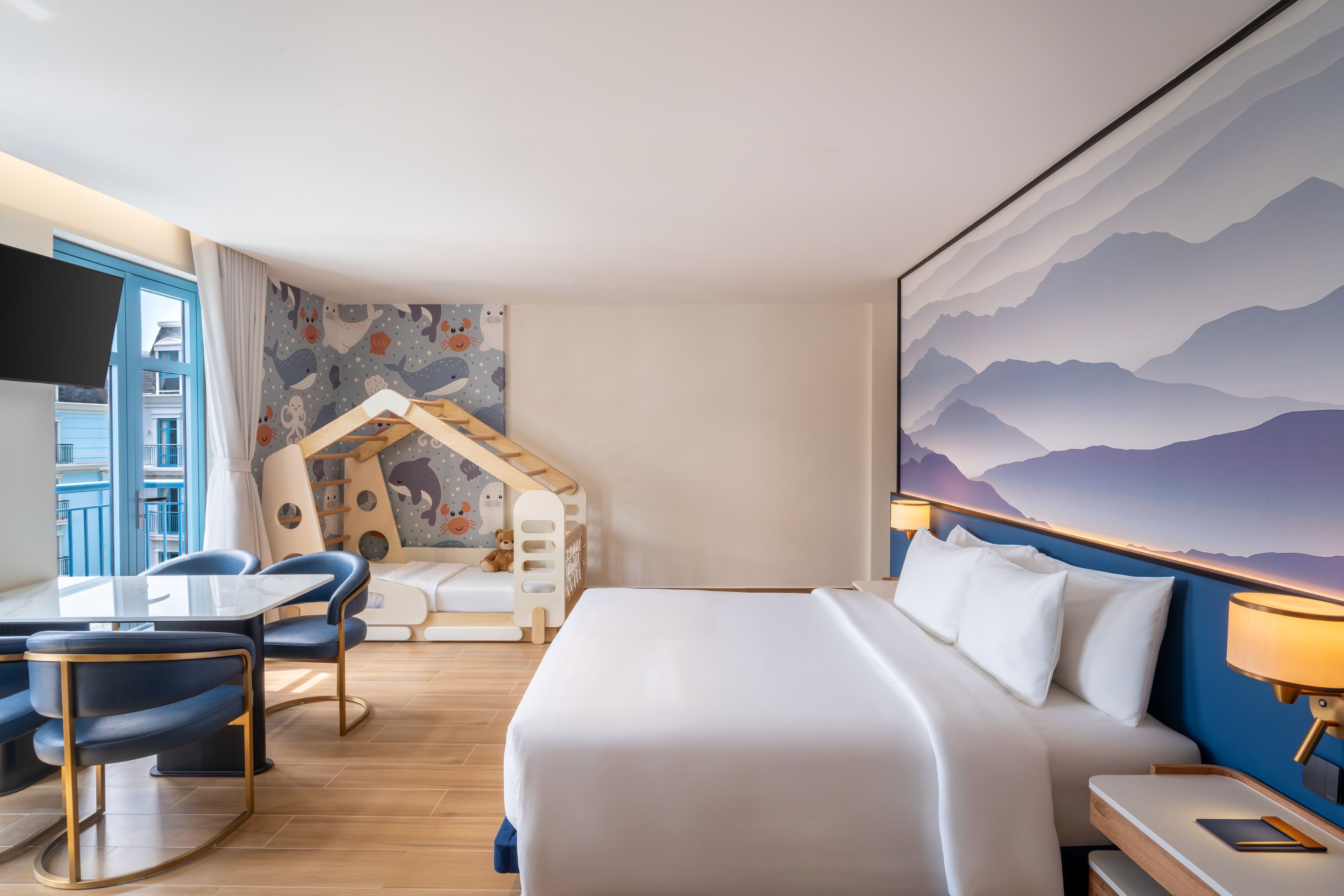 Una habitación de hotel con cama, escritorio, silla, una casita de juegos y un cuadro grande en la pared.