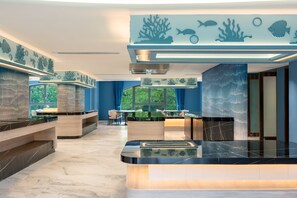Ein modernes Interieur mit einer zentralen Rezeption, einer Sitzecke und Wandbildern mit Meeresmotiven.
