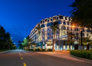 Un hotel a più piani con facciata moderna, situato all'angolo di una strada alberata da palme.
