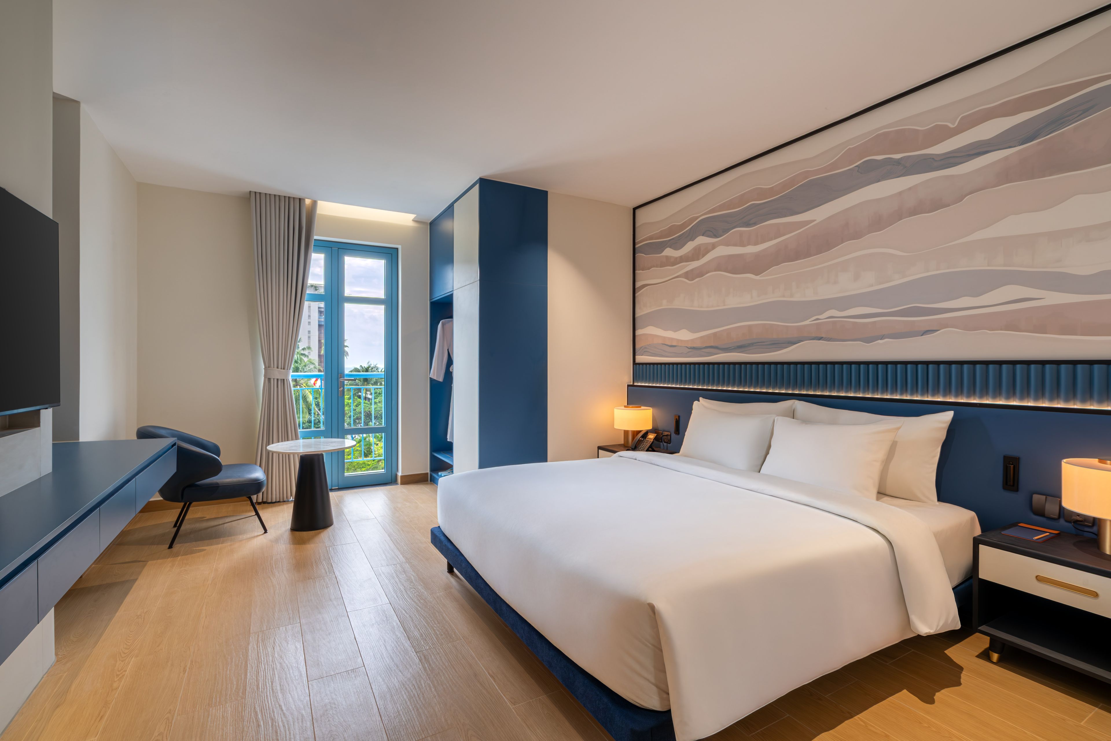 Habitación de hotel con una cama grande, un escritorio, una silla, una mesita y vistas al exterior a través de una ventana.