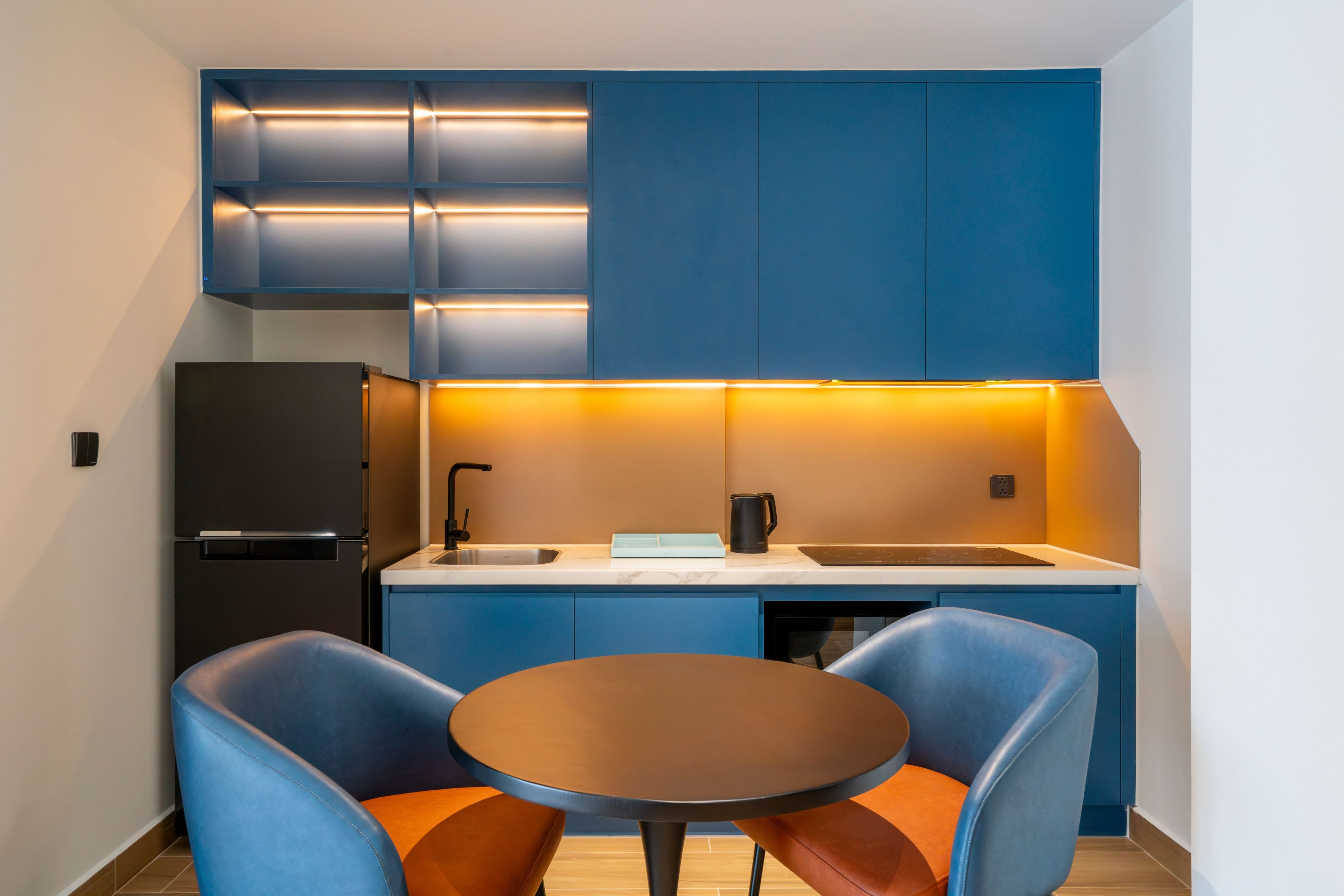 A compact kitchen with blue cabinets, a black refrigerator, a sink, and a round table with two chairs.