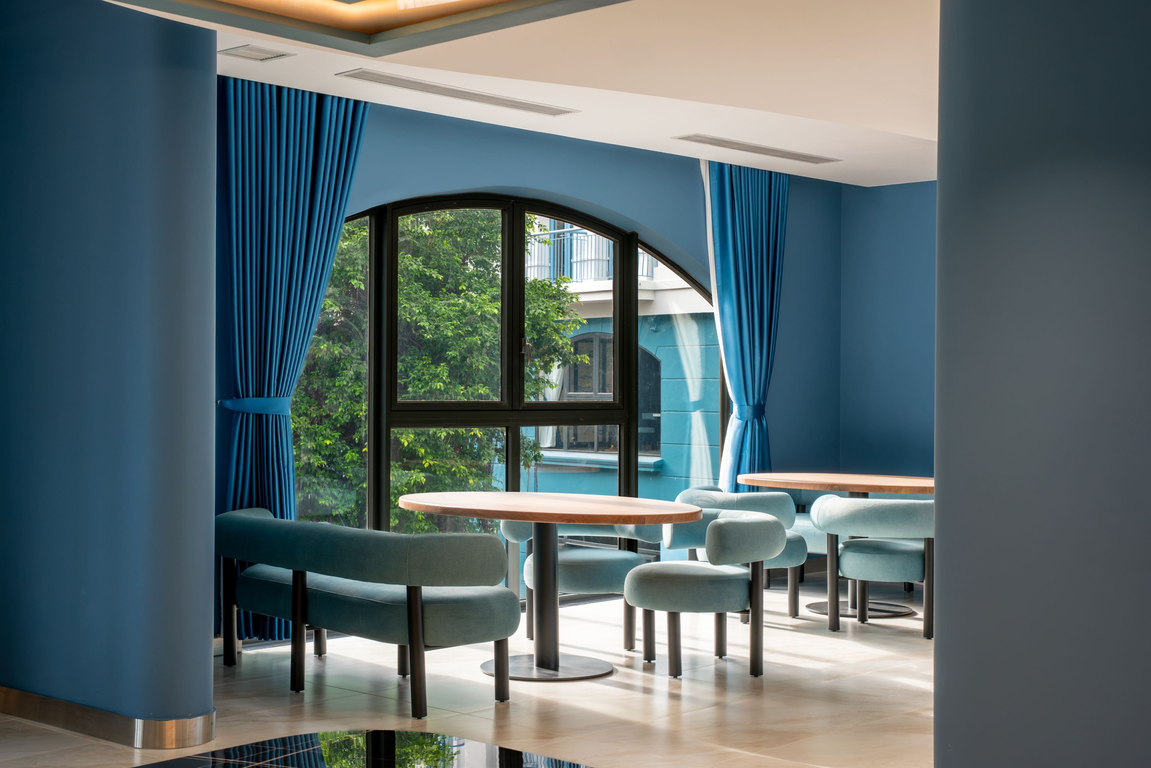 A modern interior with a large arched window, blue curtains, and a seating area with round tables and chairs.