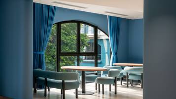 Interior moderno com uma ampla janela em arco, cortinas azuis e um espaço de estar com mesas e cadeiras redondas.