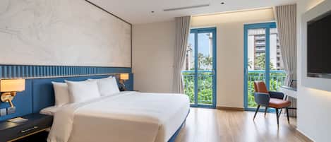 A hotel room with a large bed, a desk with a chair, a balcony with a view, and a large abstract painting on the wall.