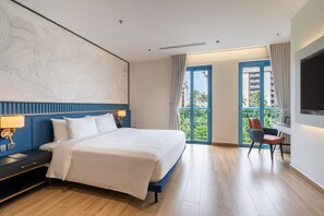 A hotel room with a large bed, a desk with a chair, a balcony with a view, and a large abstract painting on the wall. - AMÉRYS Hotel Phu Quoc (Phu Quoc)