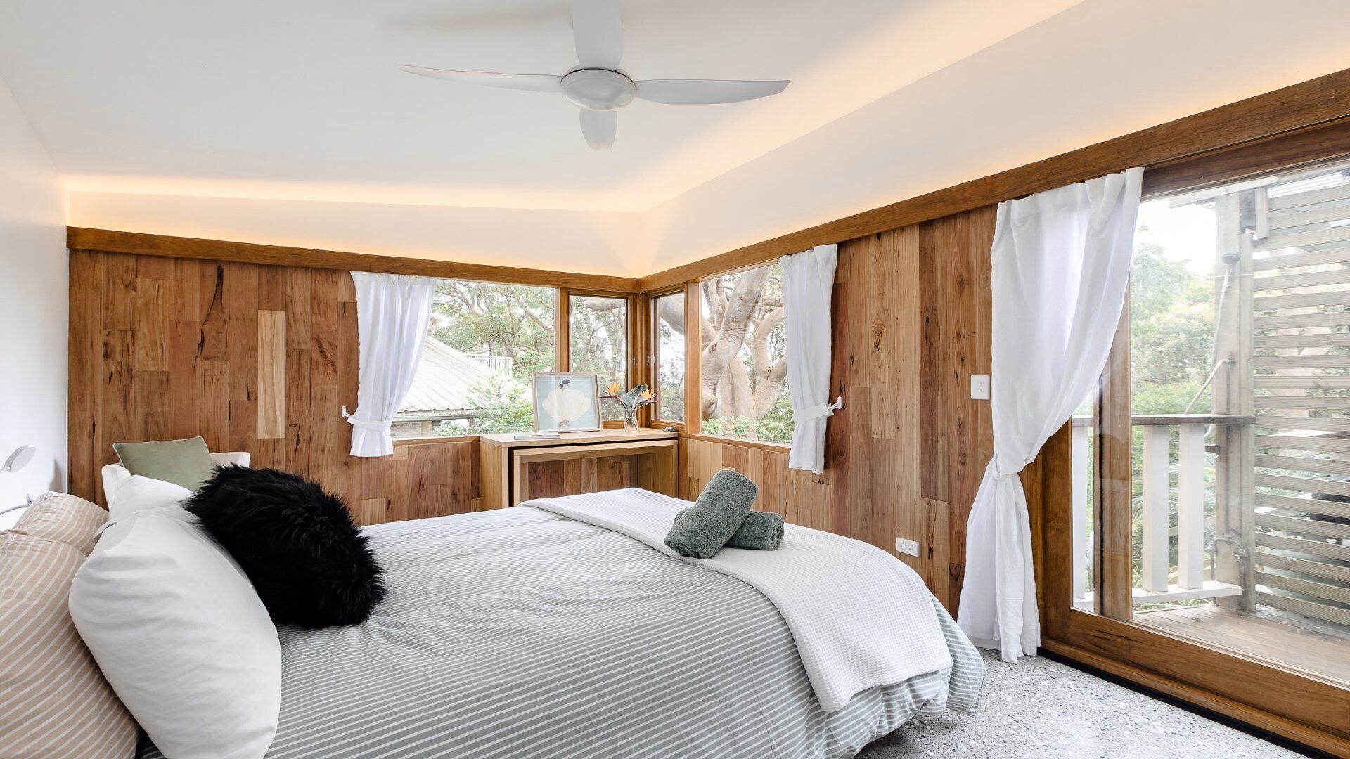 Une chambre avec un grand lit, des murs en bois, un ventilateur de plafond et une vue sur l’extérieur.