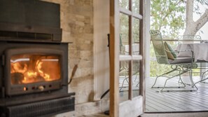 A wood-burning stove in a room with a stone wall, a glass door leading outside, and a metal chair with cushions. - Cottage plus grand/parents retreat (MACMASTERS BEACH)
