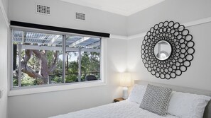 A bedroom with a large window, a round mirror, and a bed with pillows. - Cottage plus grand/parents retreat (MACMASTERS BEACH)