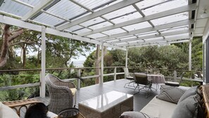 A covered outdoor area with wicker furniture, a glass-top table, and a view of the surrounding greenery. - Cottage plus grand/parents retreat (MACMASTERS BEACH)