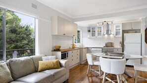 A modern kitchen with white cabinetry, a dining area with a round table and chairs, and a leather sofa with a yellow pillow. - Cottage plus grand/parents retreat (MACMASTERS BEACH)