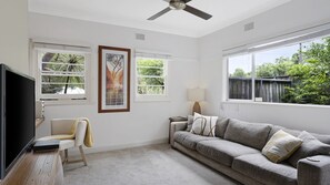 A living room with a grey sofa, a television, and two windows with blinds. - Cottage plus grand/parents retreat (MACMASTERS BEACH)