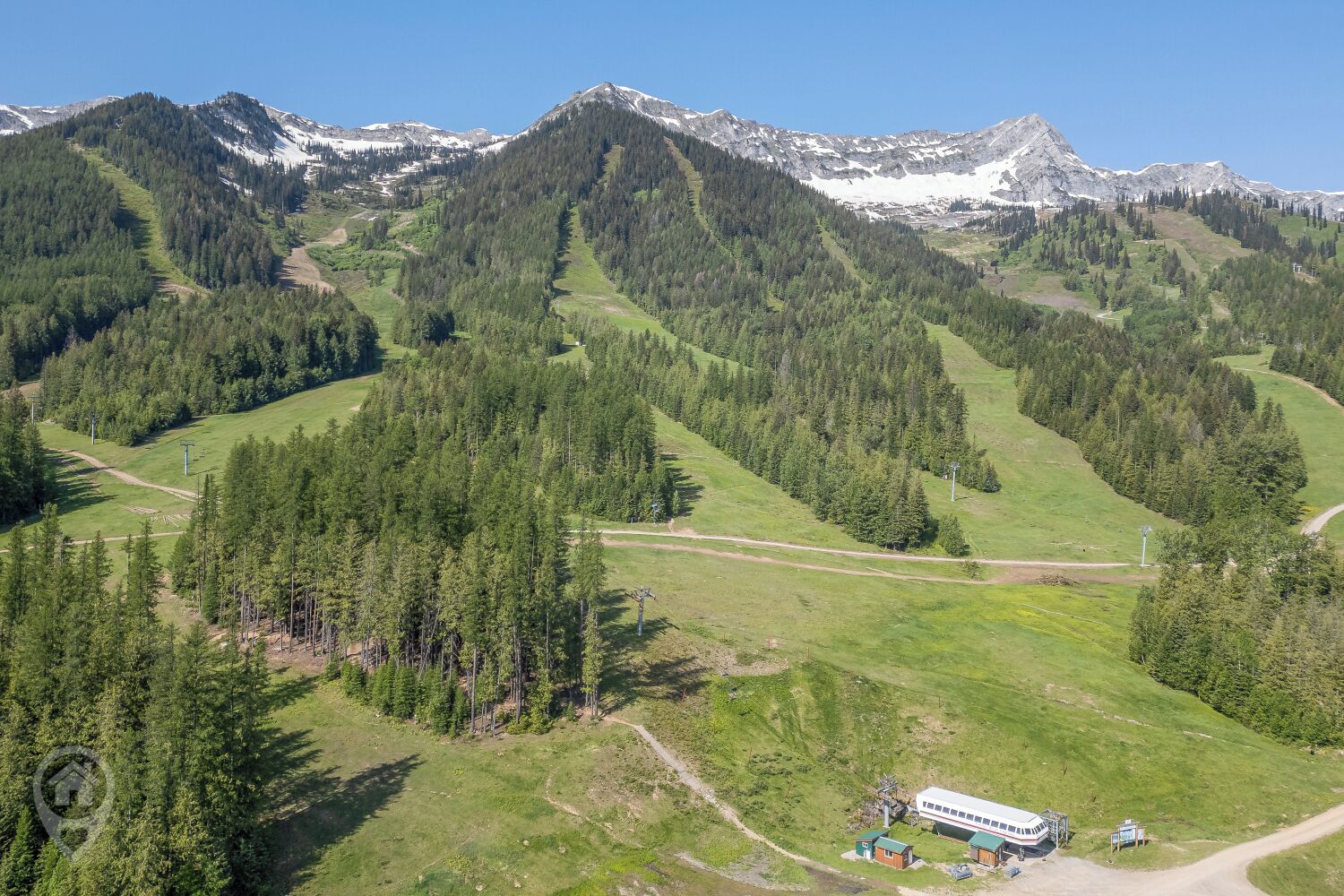 A mountainous landscape with a small building and a bus, surrounded by dense forests and snow-capped peaks.
