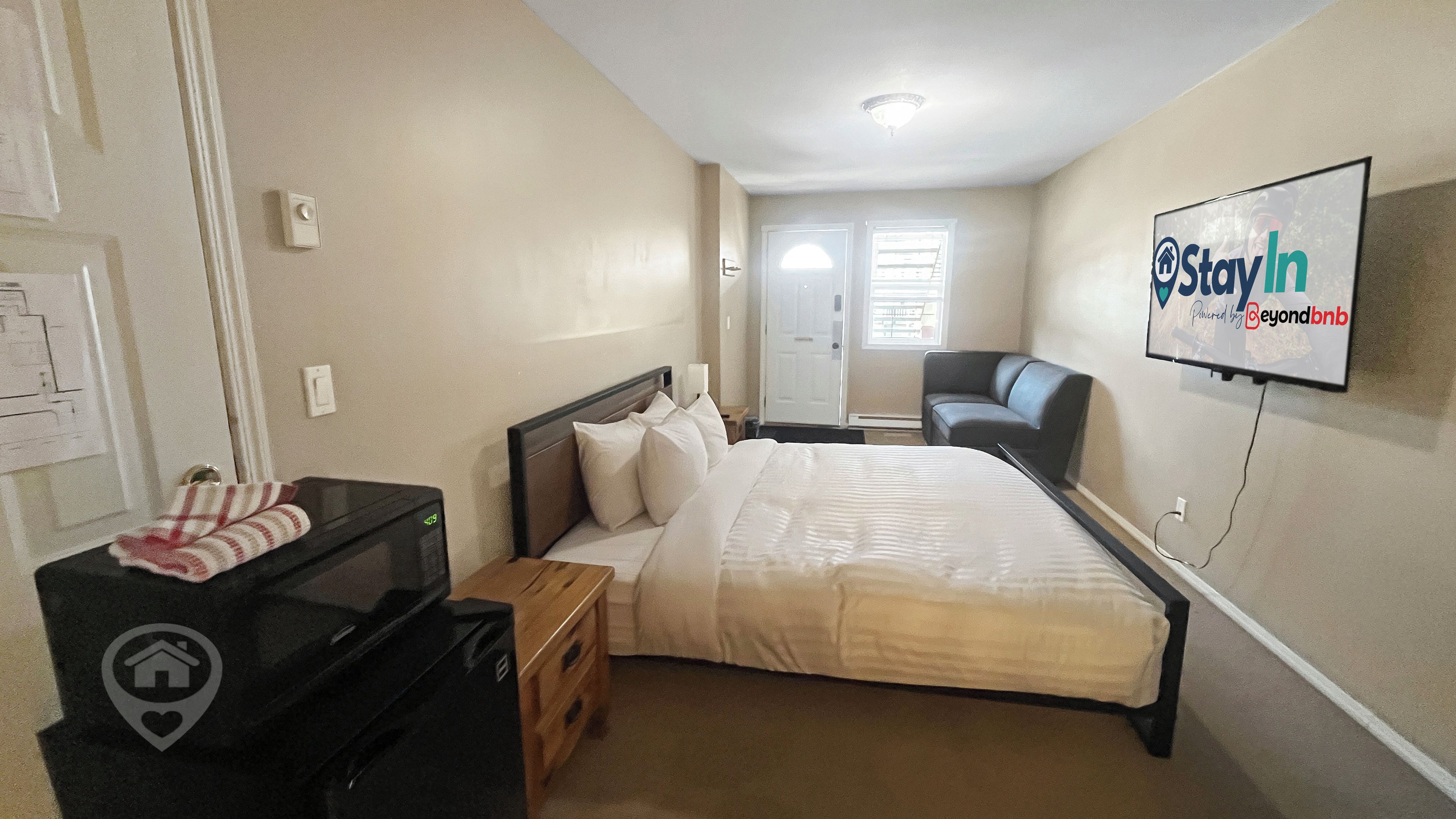 A hotel room with a bed, a desk, a chair, a TV, and a sign on the wall.