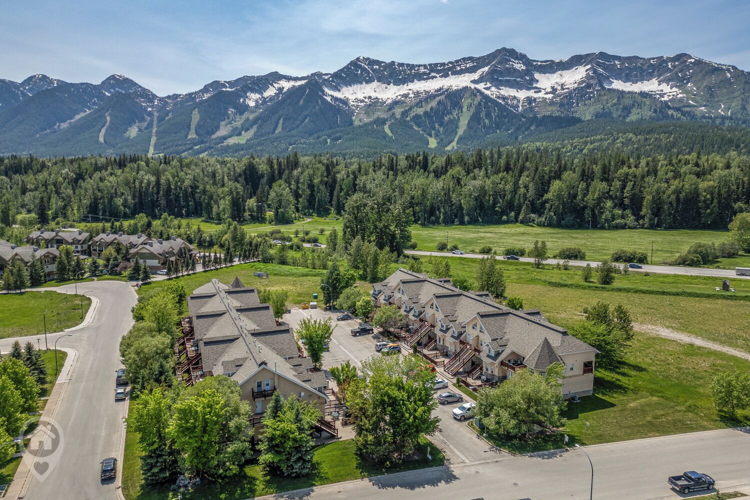 A residential area with a row of houses, a curved road, and a mountain range in the background.