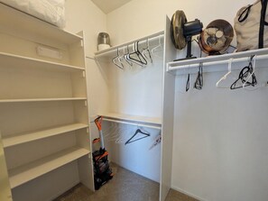 Ein begehbarer Kleiderschrank mit offenen Regalen, einem Staubsauger und aufgehängter Kleidung.